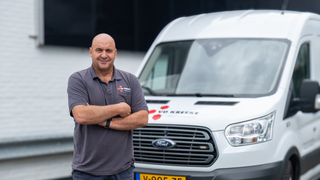 Michel Hofman, Leiter der Ausrüstungsabteilung der Van de Kreeke Group, steht vor einem Bus mit dem Logo von Van De Kreeke und lächelt.